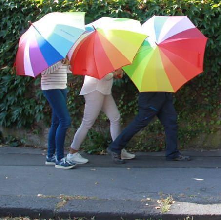 Drei Personen mit Regenschirmen gehen hintereinander her